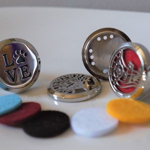 K&ouml;nnte beinhalten: Ein Set mit Auto-Lufterfrischern in verschiedenen Designs, darunter ein Pfotenabdruck mit dem Wort "LOVE", ein Lebensbaum und ein dekoratives Design. Das Set enth&auml;lt au&szlig;erdem sechs Filzpads in verschiedenen Farben: Blau, Rot, Schwarz, Wei&szlig; und Gelb.