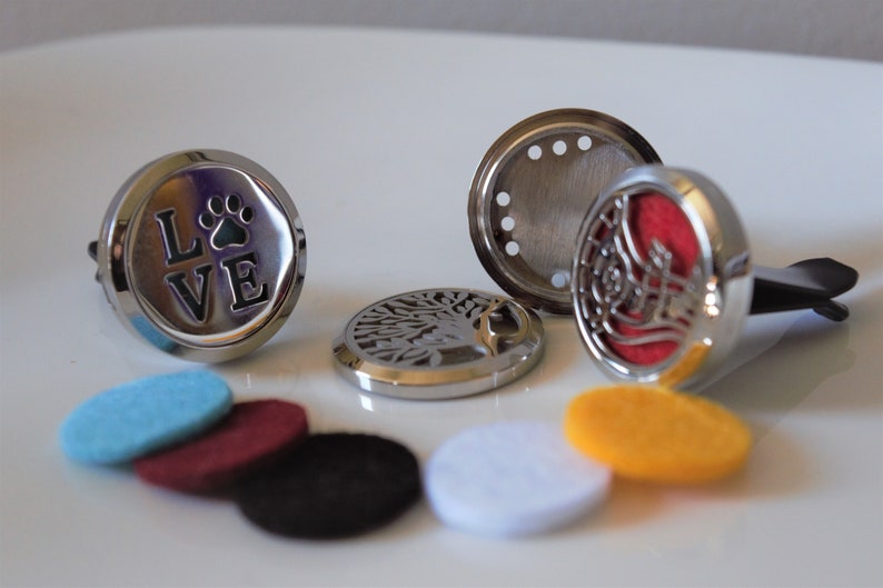 K&ouml;nnte beinhalten: Ein Set mit Auto-Lufterfrischern in verschiedenen Designs, darunter ein Pfotenabdruck mit dem Wort "LOVE", ein Lebensbaum und ein dekoratives Design. Das Set enth&auml;lt au&szlig;erdem sechs Filzpads in verschiedenen Farben: Blau, Rot, Schwarz, Wei&szlig; und Gelb.