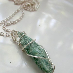 May include: A silver chain necklace with a wire-wrapped green gemstone pendant.