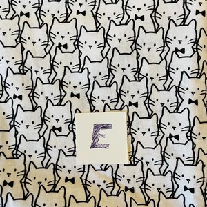 Pode incluir: Tecido branco com um padr&atilde;o repetido em preto e branco de gatos usando gravatas borboleta. A letra "E" est&aacute; escrita em roxo em um cart&atilde;o branco.