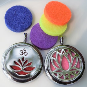 May include: Two silver locket style essential oil diffusers with a lotus flower design. One diffuser has a red lotus flower and the word "Om" in the centre. The other diffuser has a pink lotus flower. The diffusers are on a white surface with four colourful felt pads.