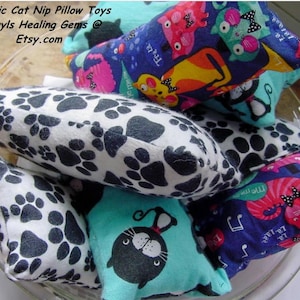 May include: A bowl filled with organic catnip pillow toys. The toys are made of fabric with various patterns, including paw prints, cats, and musical notes. The toys are all different sizes and shapes.