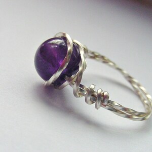May include: A silver wire ring with a purple amethyst gemstone. The wire is twisted and wrapped around the stone.