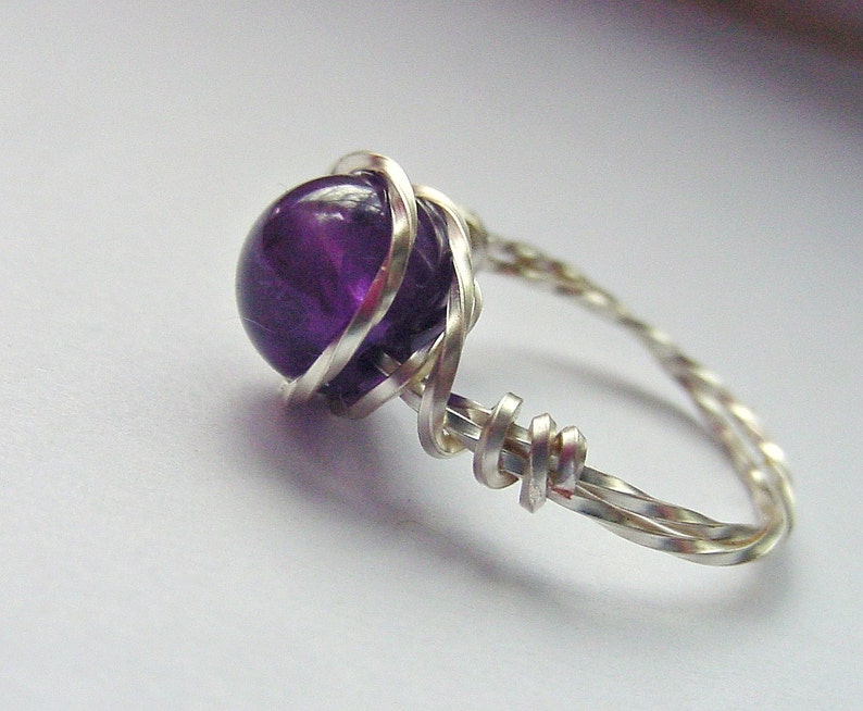 May include: A silver wire ring with a purple amethyst gemstone. The wire is twisted and wrapped around the stone.