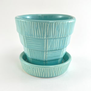 May include: A turquoise ceramic plant pot with a matching saucer. The pot features a tiered, tapered silhouette with a textured surface consisting of alternating vertical and horizontal embossed lines that create a woven, basket-like appearance.