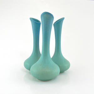 May include: Three ceramic vases in shades of blue and turquoise. Each vase has a rounded base, a slender neck, and a flared opening. The vases are arranged closely together, creating a visually appealing display. The background is plain white.