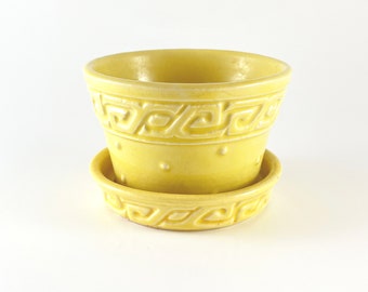 May include: A yellow ceramic planter with a matching saucer. The planter has a geometric design around the top and bottom and a dotted pattern in the middle.