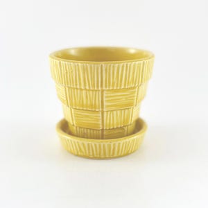 May include: A yellow ceramic planter with a matching saucer. The planter has a textured, basket-weave design. The planter is approximately 3.5 inches tall and 4 inches in diameter. The saucer is about 4 inches in diameter.