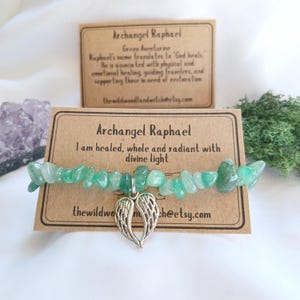 May include: A green aventurine stone bracelet with a silver angel wing charm. The bracelet is accompanied by two cards with the text "Archangel Raphael" and the phrase "I am healed, whole and radiant with divine light".