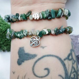 May include: Two green agate chip bracelets with a silver tree of life charm. The bracelets are stacked on a person's wrist.
