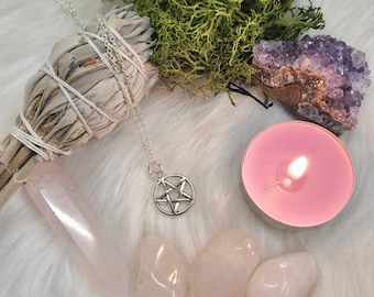 Può includere: Una collana con un pentagramma d'argento, un bastoncino di salvia bianca, cristalli di quarzo rosa, una candela rosa accesa e un ammasso di ametista viola.