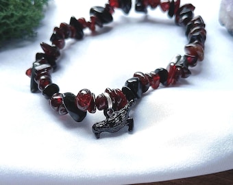 May include: A stretch bracelet composed of irregular, tumbled chip beads in deep red garnet and glossy black obsidian. The bracelet features a single black metal charm shaped like a bird, attached with a small silver-toned jump ring.