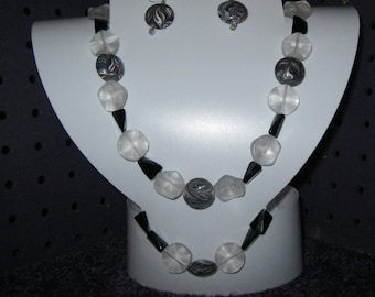 May include: A white display bust with a black and white beaded necklace and matching earrings. The necklace is made of clear and black beads.
