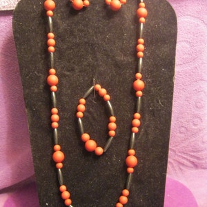 May include: A black necklace with red beads and matching earrings and bracelet. The necklace is on a black display stand.