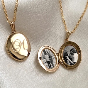 May include: Two gold-toned oval lockets on delicate matching chains. One locket is closed and features an engraved script letter M on the front. The second locket is open, revealing two small black and white photographs of people inside.