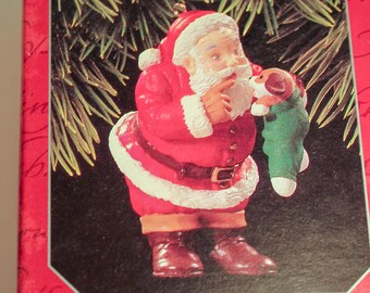 May include: A Hallmark Keepsake Collector's Club Christmas ornament in a red box. The ornament depicts Santa Claus in a red suit holding a green stocking with a puppy inside. The box reads "New Christmas Friend 1998 Membership Ornament."
