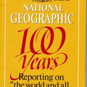 May include: A yellow magazine cover with the title "NATIONAL GEOGRAPHIC" in white text. The cover features a red handwritten number "100" and the word "Years" in red. The text "Reporting on "the world and all that is in it." - ALEXANDER GRAHAM BELL, 1914" is printed in black.