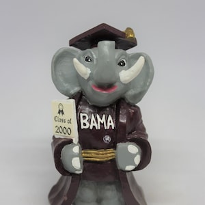 以下が含まれることがあります： 卒業ガウンと帽子をかぶった灰色の象の置物で、