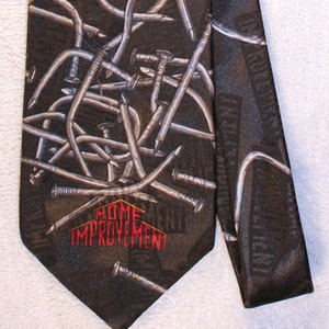 May include: A black silk tie featuring a pattern of silver nails and the text "HOME IMPROVEMENT" in red.