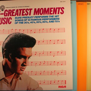 May include: A vintage vinyl record album cover featuring Elvis Presley with the title "Elvis - Greatest Moments in Music". The cover is white with red and black text. The album cover features a photo of Elvis Presley with a black and white background. The album cover also includes a musical staff with red notes.