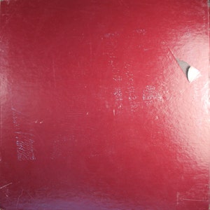 May include: A solid red vinyl record album cover with a small white sticker in the upper right corner.