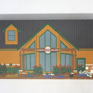 May include: A wooden model of a building with a green roof and a sign that reads "Clock & Curio Gallery". The building has a large window in the front and a smaller window on the side. There are flowers and bushes in front of the building.