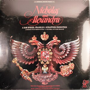 May include: A black vinyl record cover with a gold and red image of a double-headed eagle with a crown on top. The text "Nicholas and Alexandra" is written in a cursive font at the top of the cover. The text "A Sam Spiegel-Franklin J. Schaffner Production" is written in a smaller font below the image. The text "A Horizon Film Presentation-A Columbia Pictures Release" is written in an even smaller font below the production text. The text "The New Philharmonia Orchestra of London" is written in a smaller font at the bottom of the cover. The text "Conducted by Marces Dods" is written in an even smaller font below the orchestra text. The text "Music Composed by Richard Rodney Bennett" is written in an even smaller font below the conductor text.