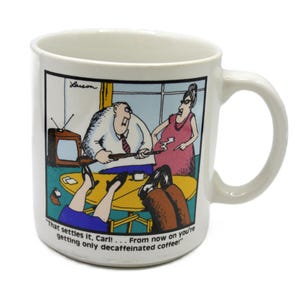 May include: A white ceramic mug featuring a Far Side cartoon by Larson. The illustration shows a person holding a smoking rifle at a table while another person points at them. The text reads, "That settles it, Carl! . . . From now on you're getting only decaffeinated coffee!"