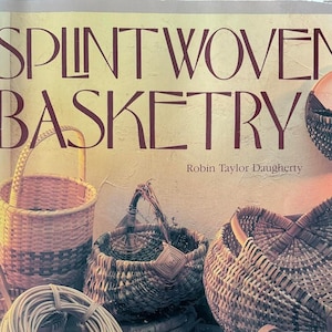 May include: The cover of a book titled "Splint Woven Basketry" by Robin Taylor Daugherty. The image features various woven baskets in different shapes and sizes, along with bundles of weaving materials. The baskets are in shades of brown and tan.