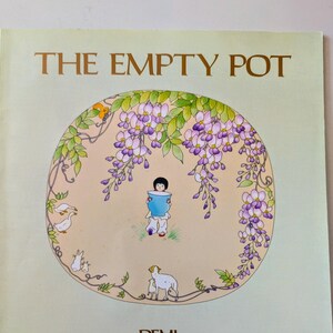 May include: A children's book titled "The Empty Pot" with a light green cover. The cover features a circular illustration of a child holding a blue pot, surrounded by wisteria and animals. The author's name, DEMI, is at the bottom.