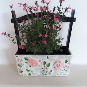 May include: A mosaic planter box with a black frame, filled with green foliage and pink flowers. The mosaic design features floral patterns in shades of pink, white, and green. The planter is a decorative item for indoor or outdoor use.