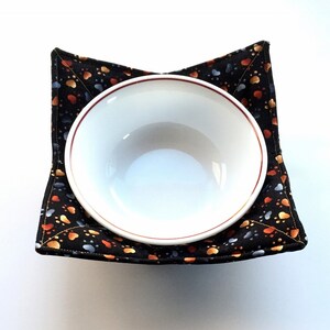 May include: A black bowl cozy with a paw print pattern. The cozy is filled with a white ceramic bowl.
