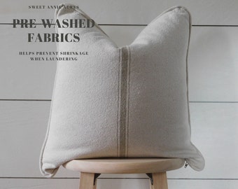 May include: A white pillow with a brown stripe down the center. The pillow is pre-washed and helps prevent shrinkage when laundering. The text "PRE WASHED FABRICS" is written in black at the top of the image. The text "HELPS PREVENT SHRINKAGE WHEN LAUNDERING" is written in black below the pillow.