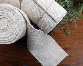 May include: Three rolls of natural-colored cotton webbing, each tied with twine. The webbing is woven with a herringbone pattern.