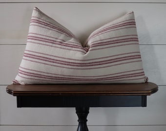 May include: A white and red striped pillow with a farmhouse style design. The pillow is sitting on a black table with a wooden top.