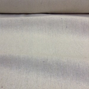May include: A close-up of a natural off-white woven fabric with a subtle texture. The fabric is folded in half, showing the smooth surface on the top and the woven texture on the bottom.