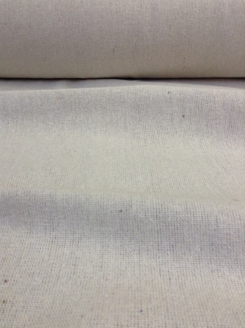 May include: A close-up of a natural off-white woven fabric with a subtle texture. The fabric is folded in half, showing the smooth surface on the top and the woven texture on the bottom.