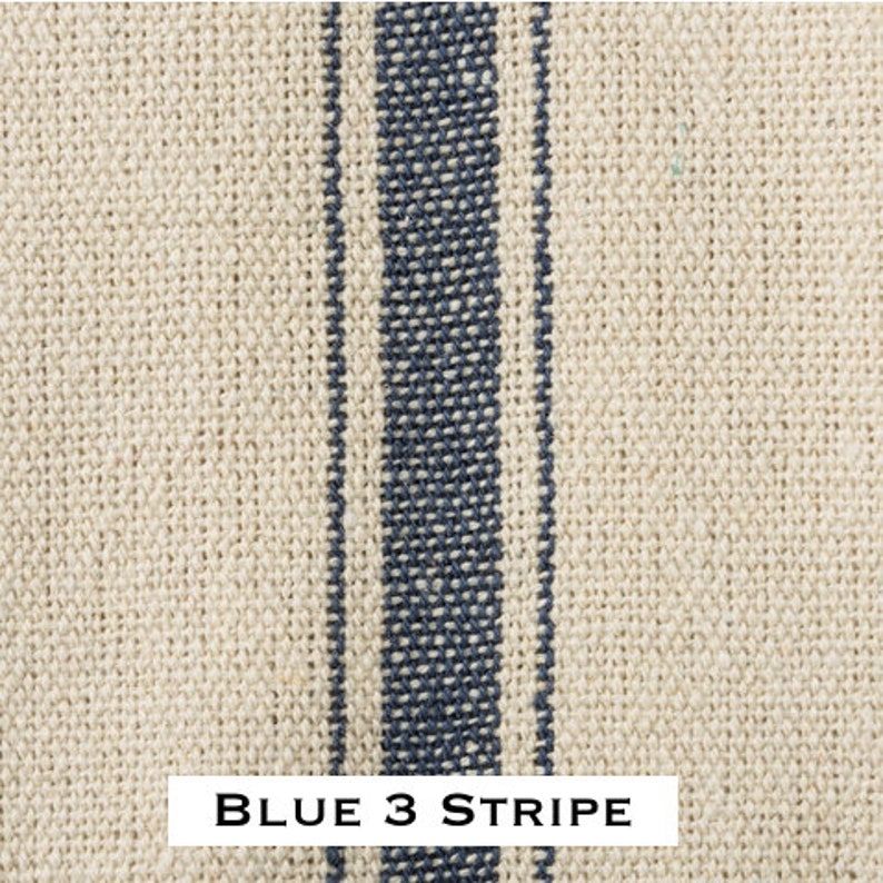 May include: Close-up of a natural linen fabric with three blue stripes. The fabric has a woven texture and is a light beige color. The stripes are a dark blue color and are evenly spaced. The text "BLUE 3 STRIPE" is printed at the bottom of the image.