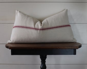 May include: A white pillow with two red stripes on a dark wooden table with a black pedestal base.