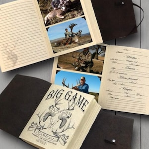 Puede incluir: Un diario encuadernado en cuero marrón con el título "Big Game Hunting Journal: Passing on the Heritage". El diario tiene páginas para registrar viajes de caza con secciones para la ubicación, la fecha, el clima, el terreno, el juego perseguido, el arma y otros detalles. El diario está abierto para revelar fotos de cazadores con su caza.