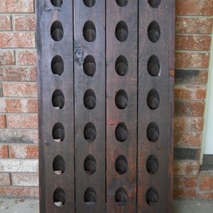 May include: A dark brown wooden wine rack with 24 slots for storing wine bottles. The rack is made of stained wood and has a rustic look.