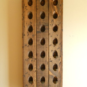 May include: A wooden wine bottle rack with 18 holes for storing wine bottles. The rack is made of natural wood with a rustic finish.