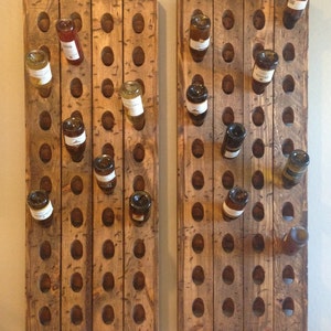 May include: Two wooden wine bottle racks mounted on a wall. Each rack has 12 rows of holes for holding wine bottles. The racks are made of rustic wood with a natural finish.
