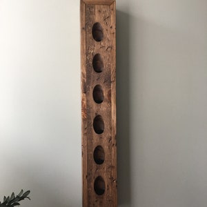 May include: A rustic wooden wine rack with six slots for bottles. The rack is stained a dark brown color and has a distressed finish.