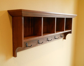 May include: A wooden wall shelf with four cubbies and six hooks. The shelf is stained a dark brown color and has a decorative trim around the top and bottom.