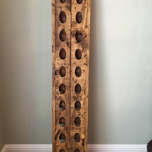 May include: A rustic wooden wine rack with a distressed finish. The rack has two rows of oval-shaped openings for holding wine bottles.