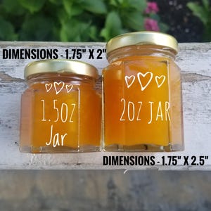 May include: Two glass jars with gold lids filled with a yellow substance. The smaller jar is labeled "1.5 oz Jar" and the larger jar is labeled "2 oz Jar". Both jars have three white hearts on the front. The dimensions of the smaller jar are 1.75 inches by 2 inches and the dimensions of the larger jar are 1.75 inches by 2.5 inches.