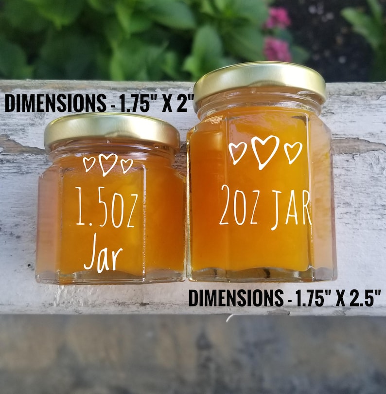 May include: Two glass jars with gold lids filled with a yellow substance. The smaller jar is labeled "1.5 oz Jar" and the larger jar is labeled "2 oz Jar". Both jars have three white hearts on the front. The dimensions of the smaller jar are 1.75 inches by 2 inches and the dimensions of the larger jar are 1.75 inches by 2.5 inches.
