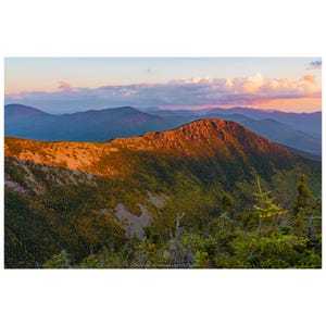 May include: A scenic landscape photograph of a mountain range at sunset. The foreground features green trees, while the middle ground shows a mountain illuminated by golden sunlight. The sky displays a gradient of pink, blue, and orange hues.