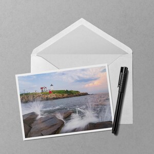 May include: A scenic photograph of a coastal landscape featuring a lighthouse on a rocky island. The image shows crashing waves, a white envelope, and a black pen, all set against a gray background. The lighthouse has a red roof.